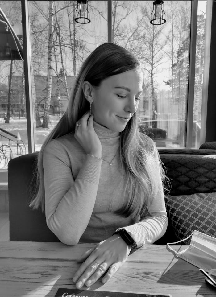 Black and white portrait of a woman sitting at a cafe table, exuding elegance and calm.