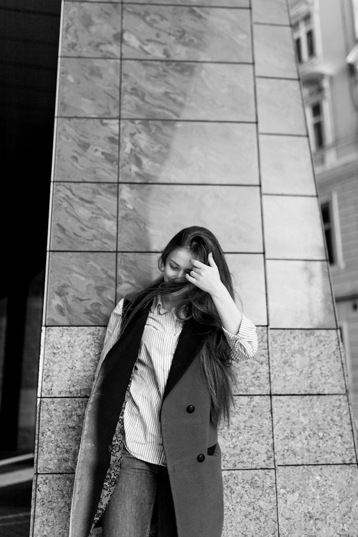 Black and white photo of a young woman posing stylishly against a modern urban wall.